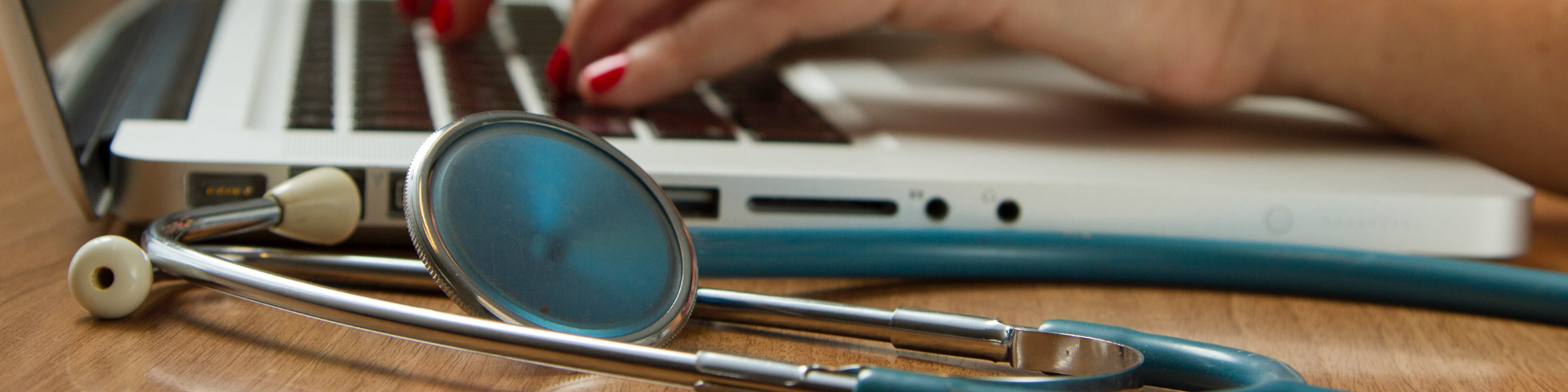 Someone typing on a laptop with a doctor's stethoscope