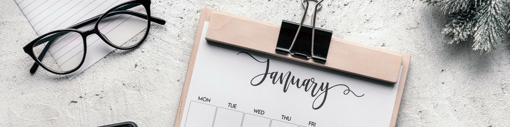 A desk layout with a calendar showing January, pencil, glasses and clock