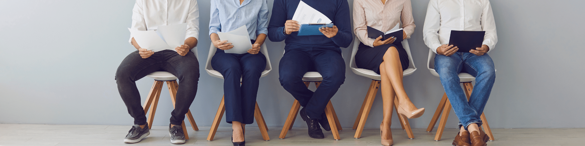 Multiple people sat in a row on chairs shown from the waist down